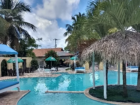 Schwimmbad des Restaurants 'El Currican' in Juan Dolio, umgeben von Palmen und Sonnenschirmen mit einem Sicht auf das Hauptgebäude des Restaurants im Hintergrund.